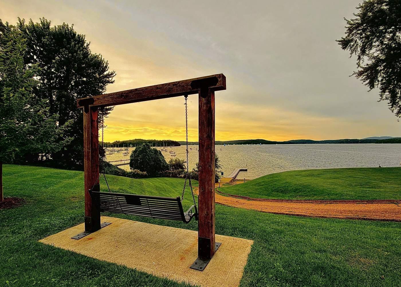 Une balançoire en bois sur une colline gazonnée surplombant la baie Malletts et ses voiliers au coucher du soleil
